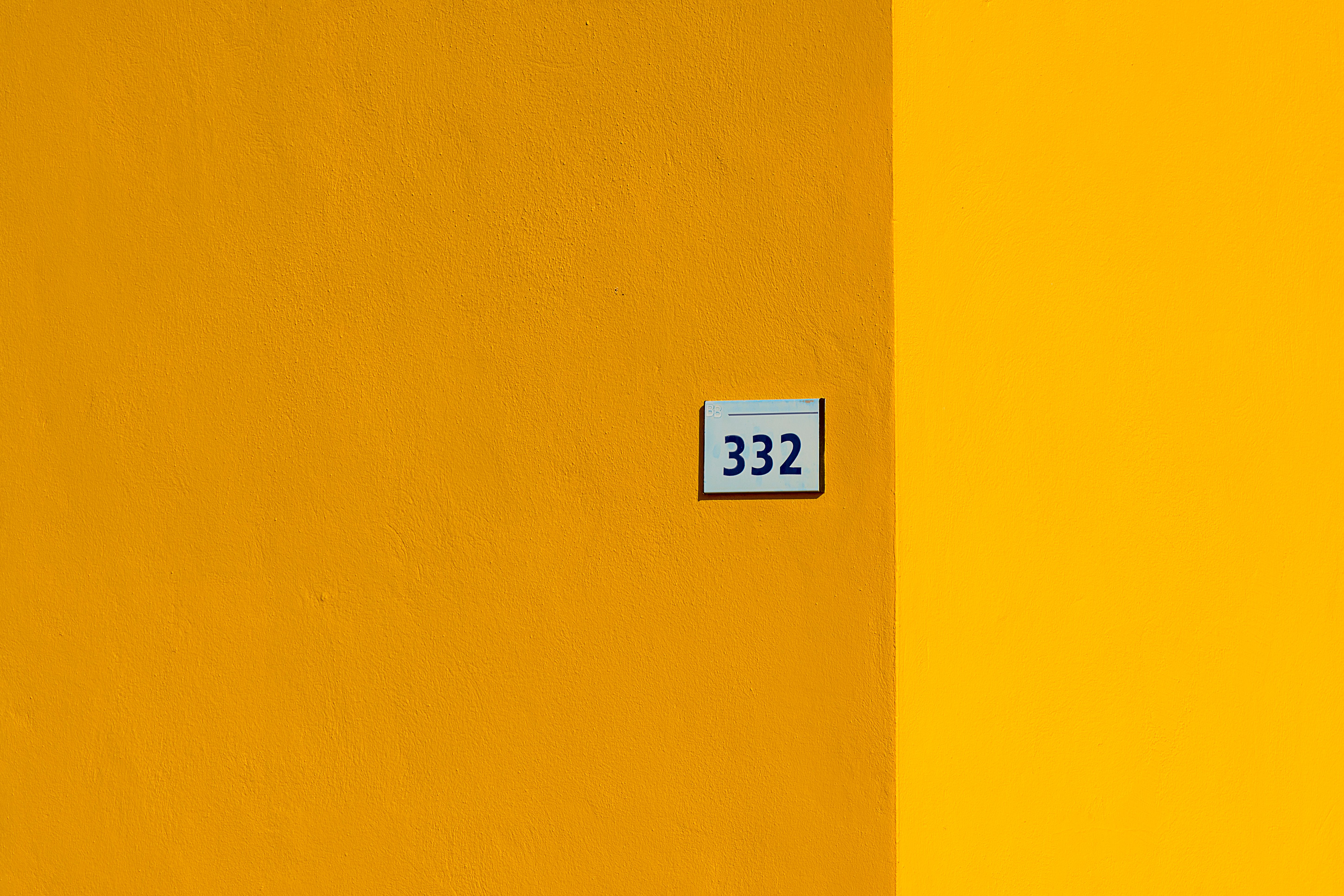 Minimalist yellow wall with number 332, showcasing vibrant color contrast.