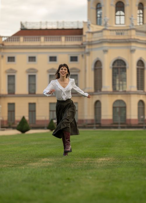 Free Smiling woman in elegant attire joyfully runs in front of a historic building in Berlin, Germany. Stock Photo