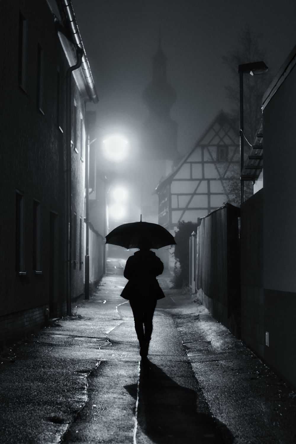 Silhouette of a person with an umbrella on a misty street at night