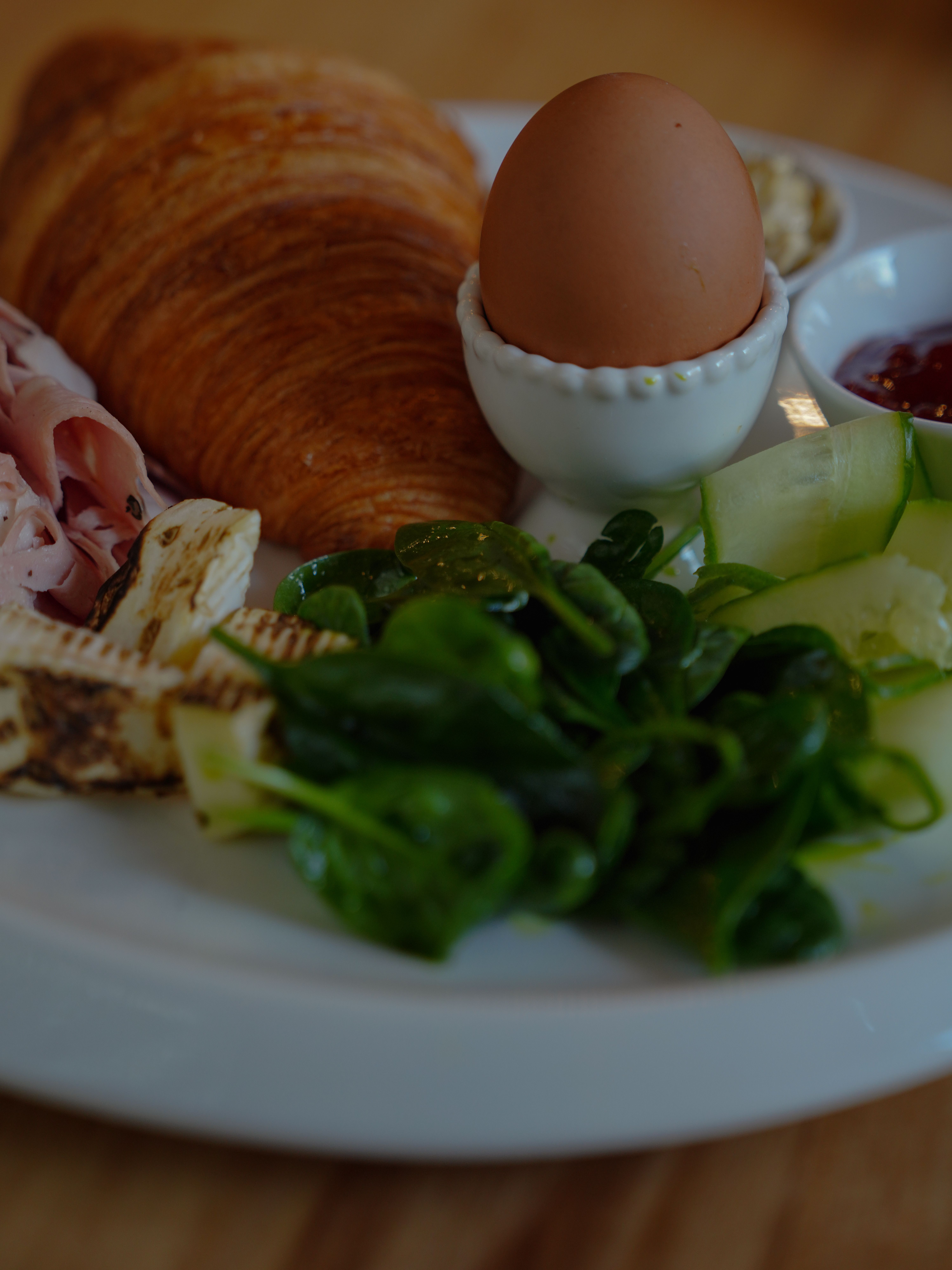 Continental breakfast plate featuring a croissant, boiled egg, greens, and cheese.