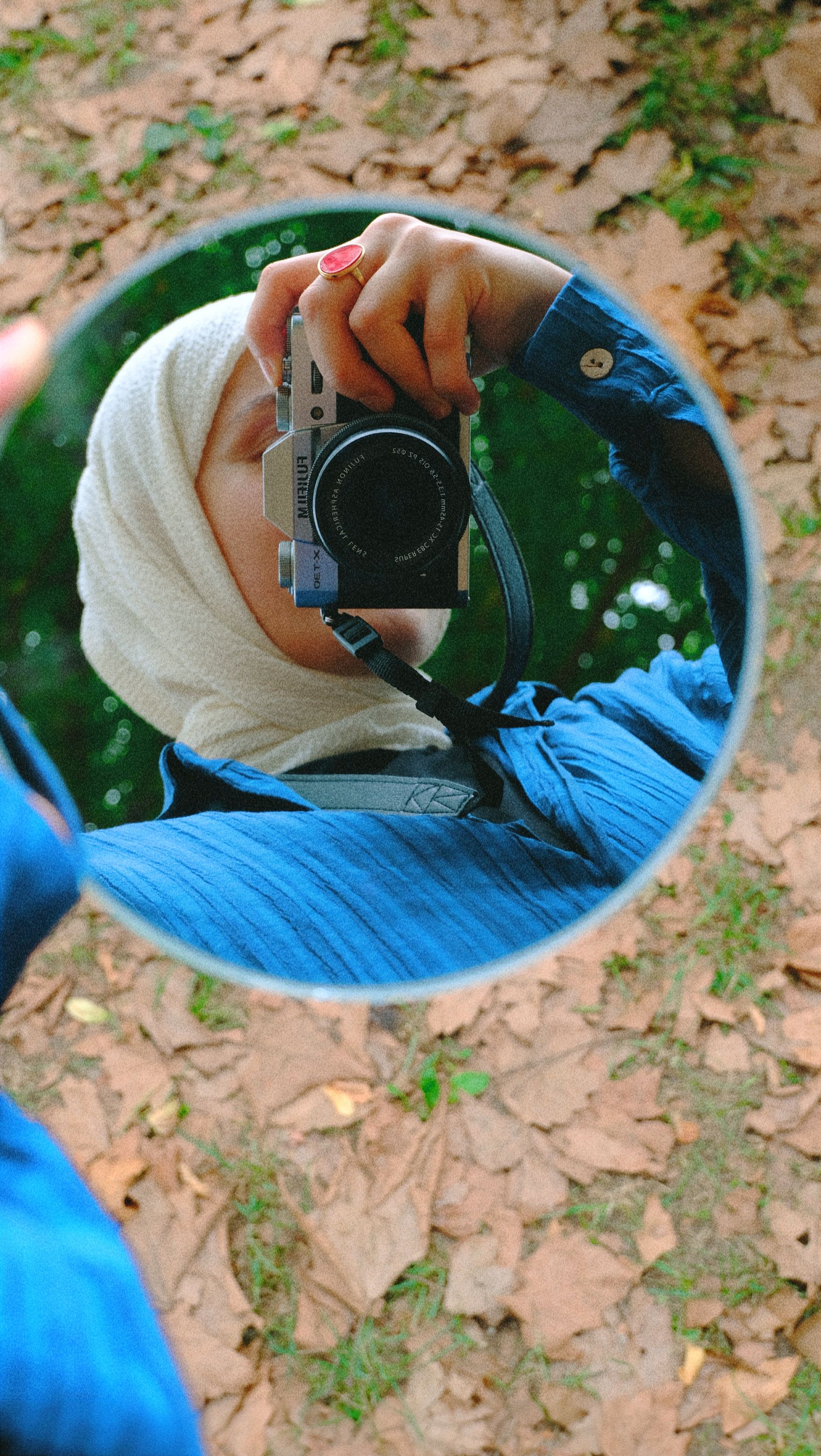 A woman in hijab photographs her reflection holding a camera in a mirror outdoors.