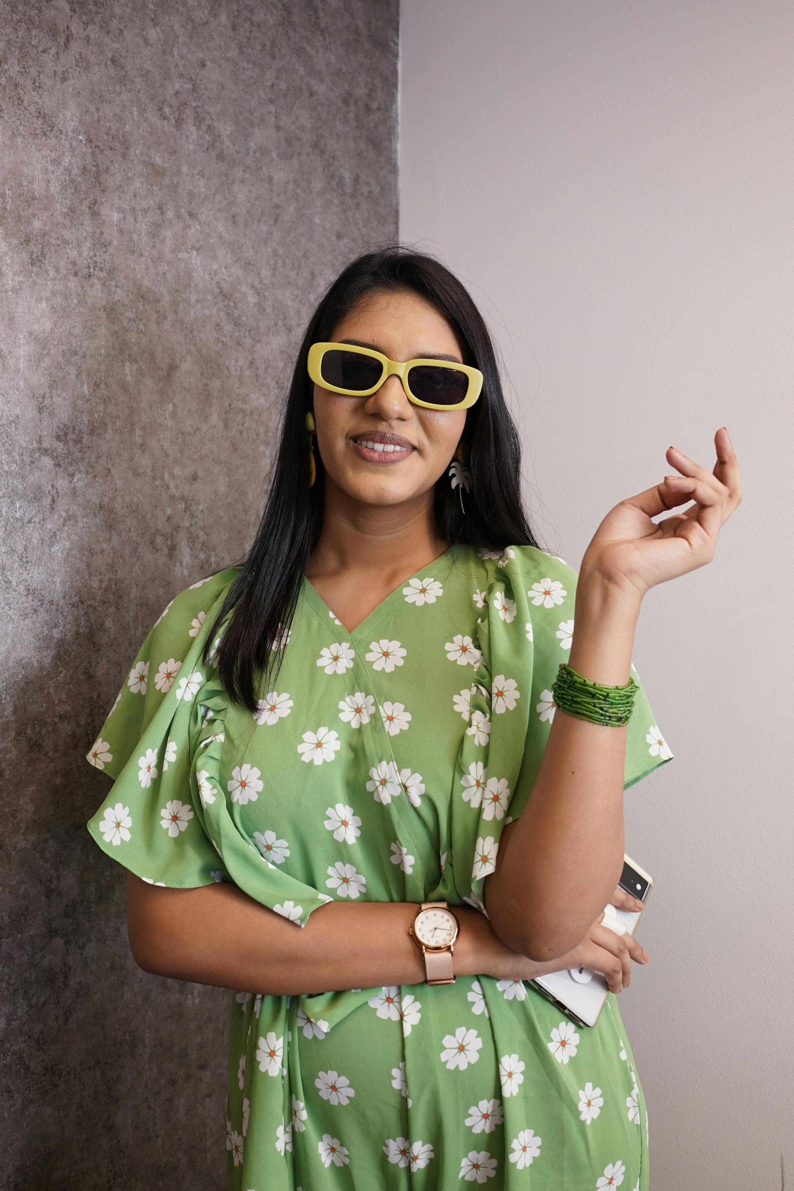 Chic portrait of a woman in sunglasses and a green dress with floral patterns, exuding confidence and style.