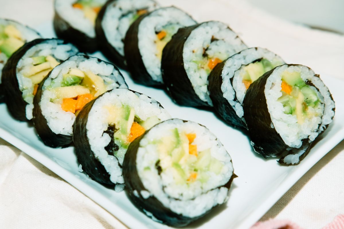 Row of sliced vegetable sushi rolls with avocado, carrot and cucumber on a white plate