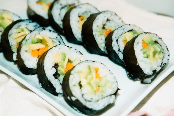 Row of sliced vegetable sushi rolls with avocado, carrot and cucumber on a white plate