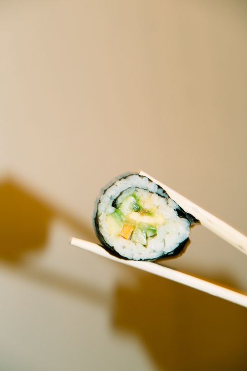 Free A close-up of a delicious sushi roll held by chopsticks, highlighting Japanese cuisine. Stock Photo