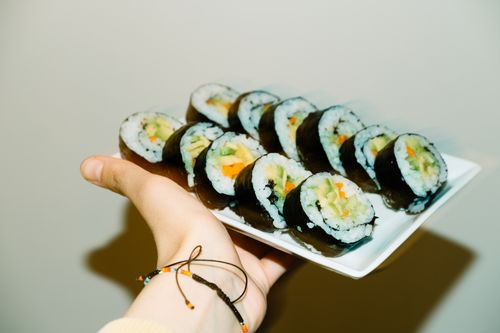 Free Close-up of vegetarian sushi rolls held on a white plate by a hand. Stock Photo