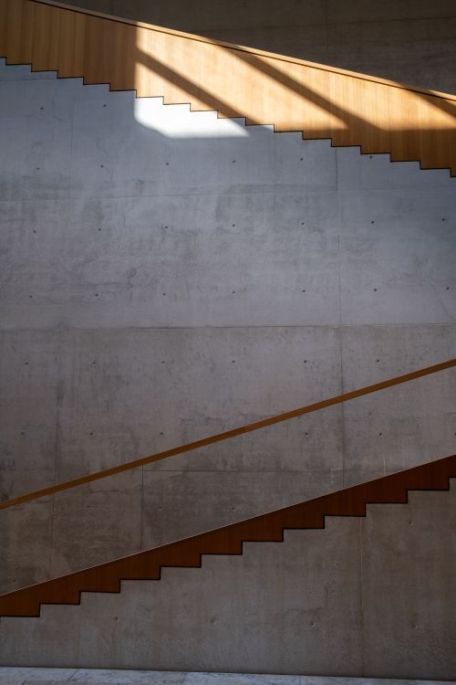 Free Contemporary minimalist staircase with concrete walls and wooden elements in sunlight. Stock Photo