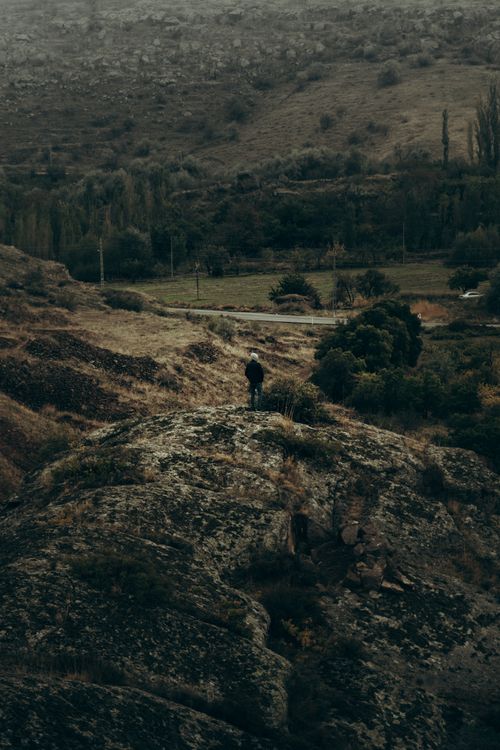 Free A lone hiker stands on a rock, gazing at the expansive valley below, capturing tranquility and adventure. Stock Photo