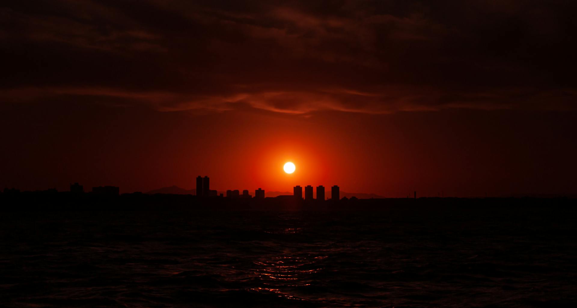 Captivating silhouette of Fortaleza skyline against a fiery sunset over the sea.