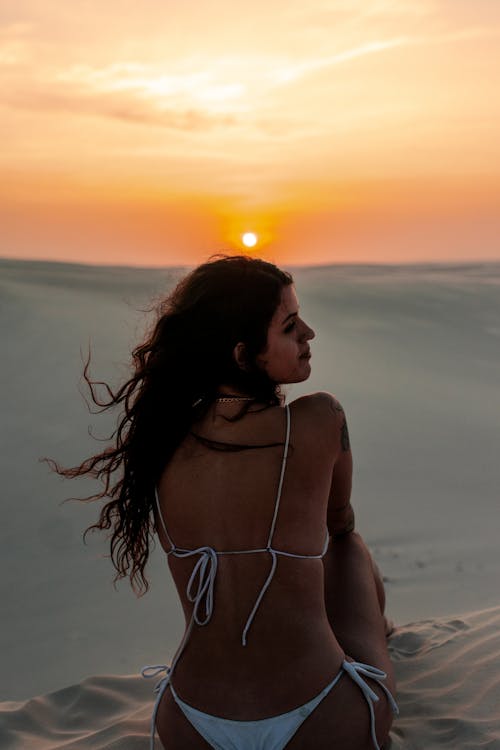 Woman in White Bikini Sitting on Desert at Sunset