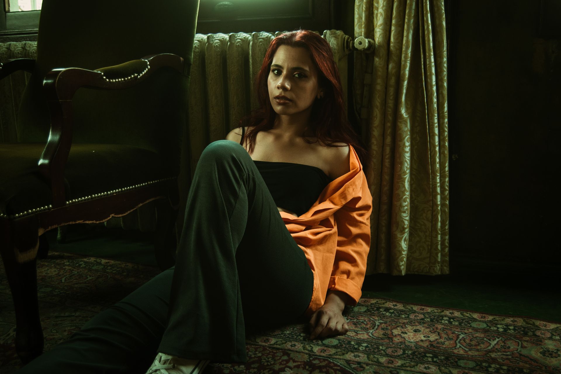 Portrait of a woman sitting on a vintage rug inside a room, wearing an orange shirt.