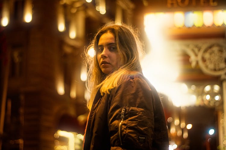 Blonde Woman In Black Jacket On Illuminated City Street At Night