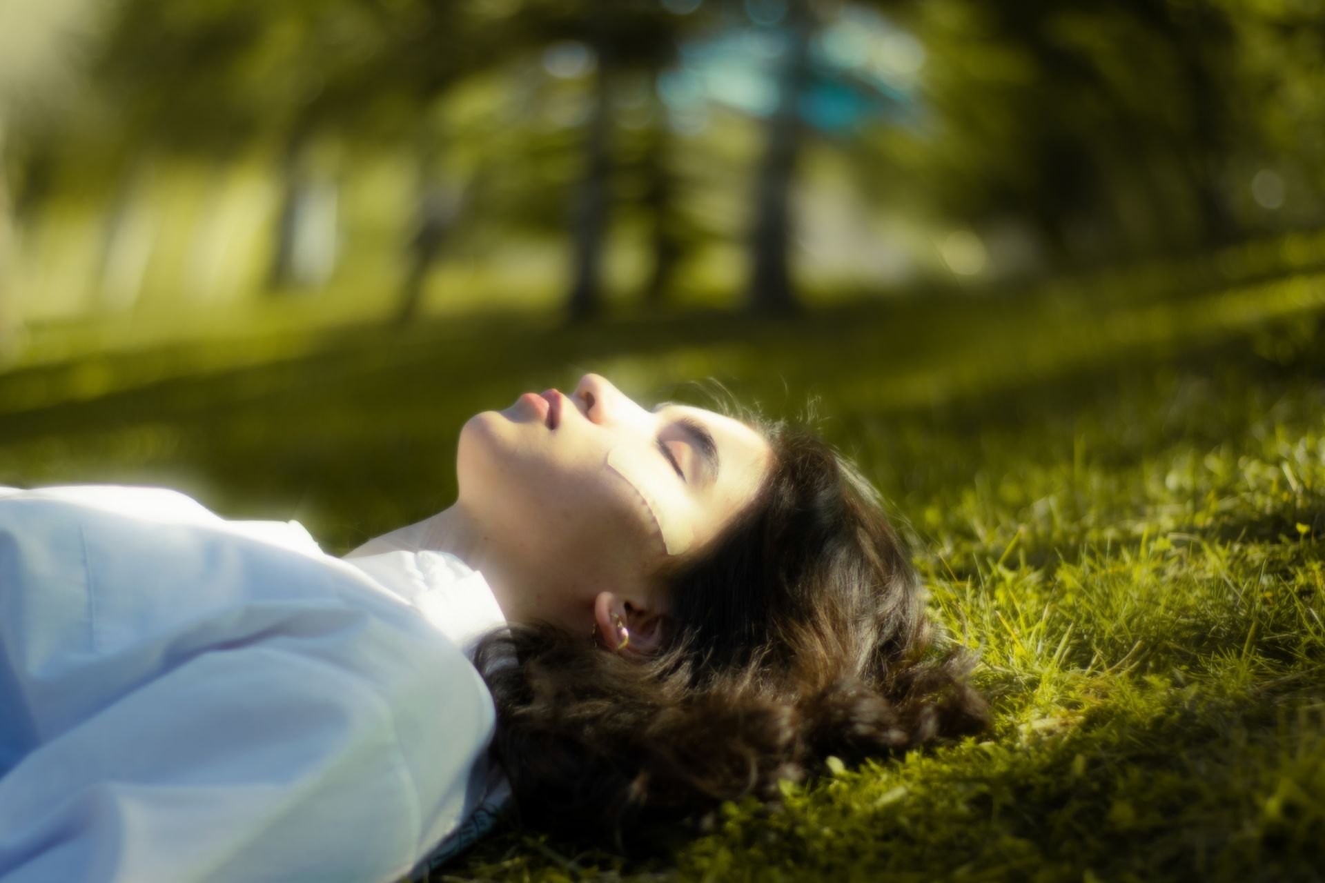 A woman lying with eyes closed in tall sunlit grass