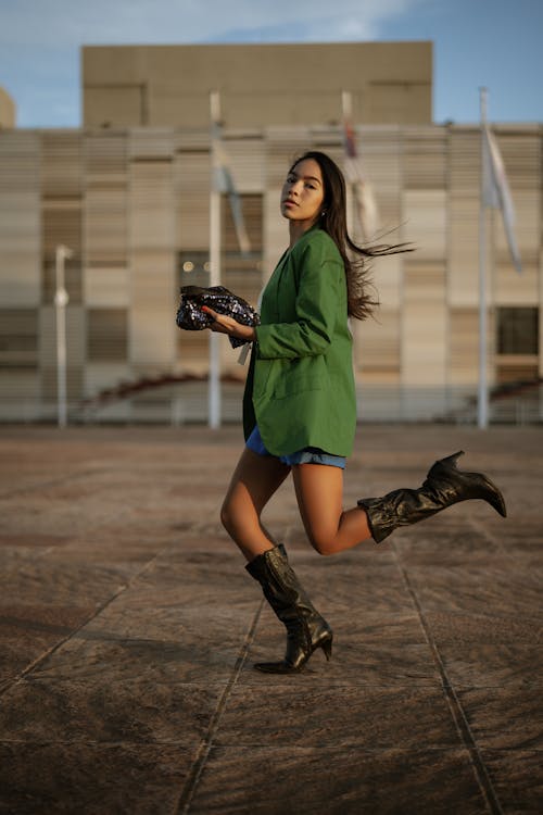 Young Woman in Green Blazer and Black Leather Boots Posing with a Black Sequin Purse