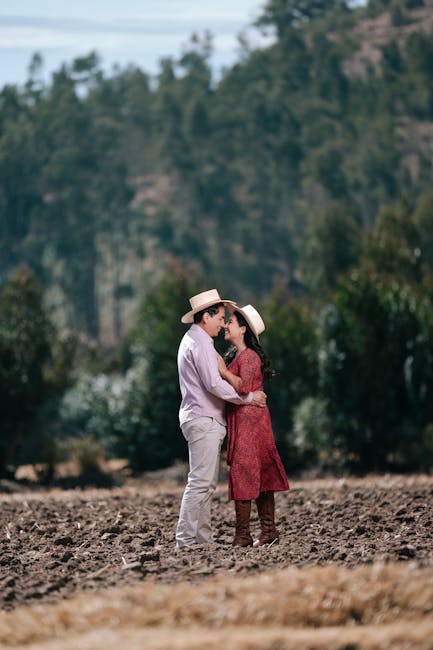 A couple embracing in a rural field wearing hats, highlighting their romantic connection.