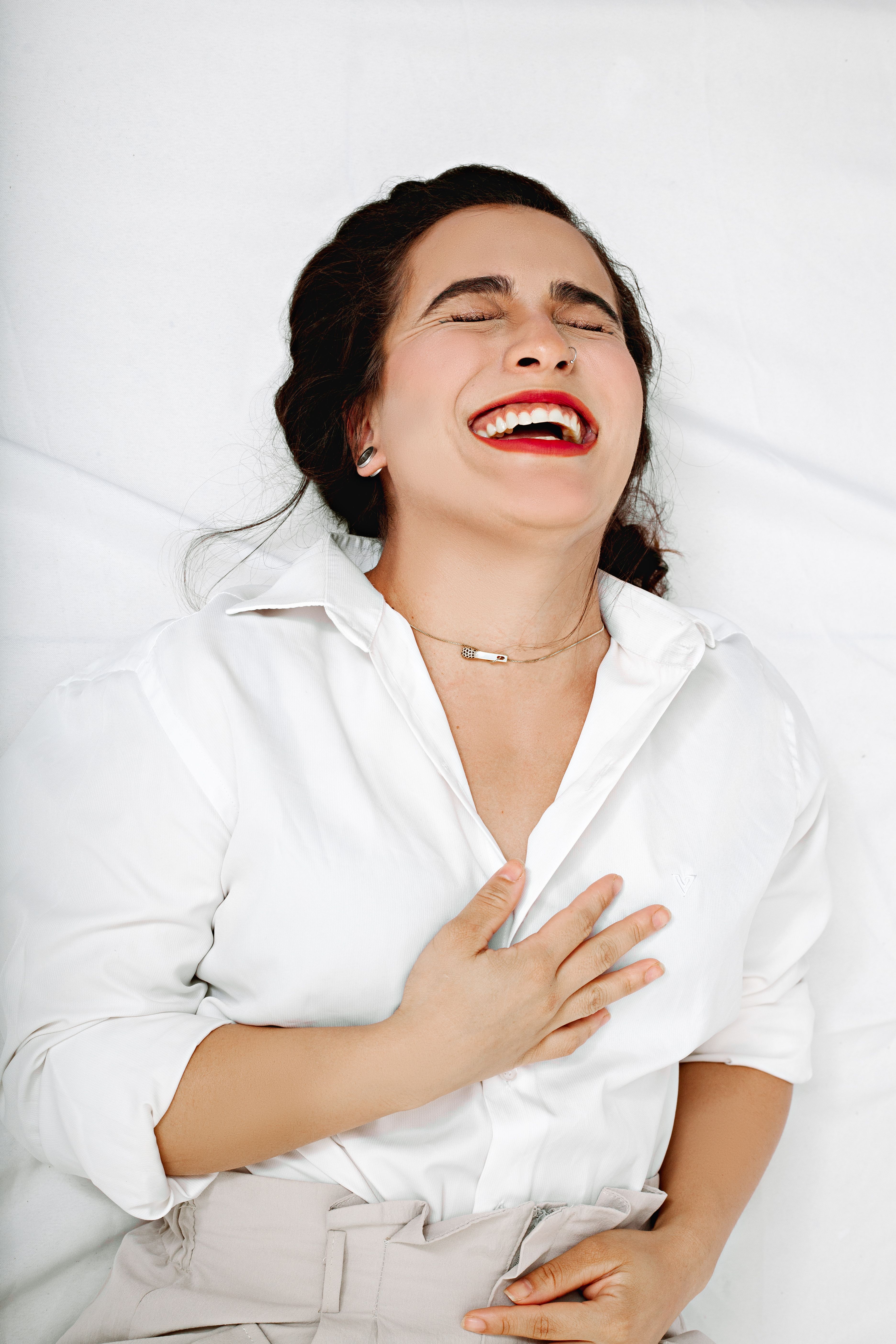 Woman in a white shirt laughing joyfully with her eyes closed, hand on her chest