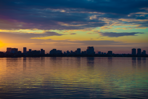 Free A stunning view of Hanoi's skyline reflecting on a calm lake during sunrise. Stock Photo