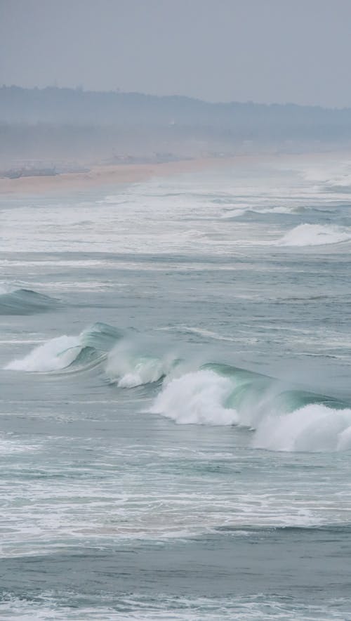 A surfer rides a wave on a beach in the rain