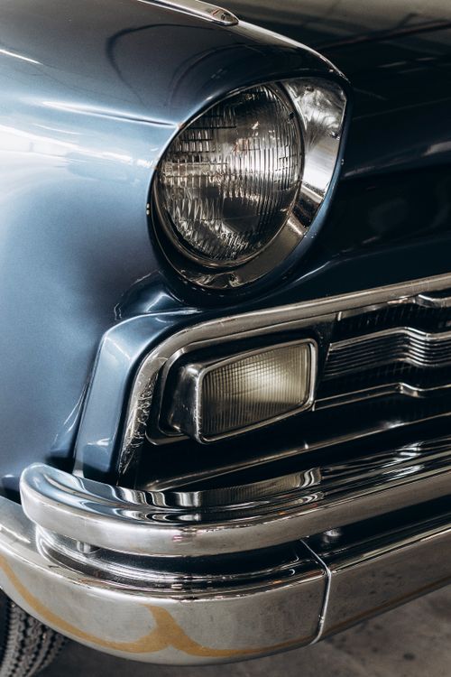 Free Detailed view of a classic blue car's headlight and chrome bumper in a garage. Stock Photo