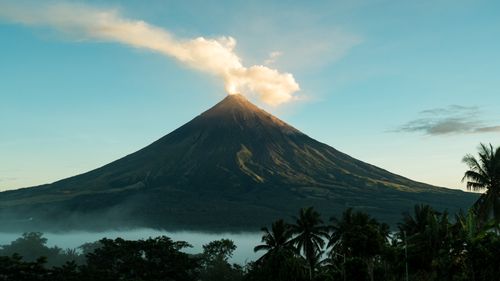 Free Stunning view of Mayon Volcano emitting smoke surrounded by lush tropical landscape in the Philippines. Stock Photo