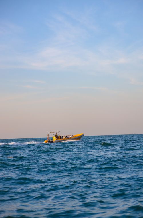 Free A motorboat speeds through the blue sea with distant Dubai skyline under a clear sky. Stock Photo
