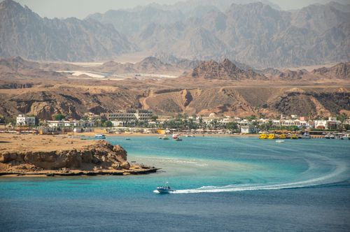 Free Beautiful coastal view with a mountain backdrop and a motorboat on the sea. Stock Photo