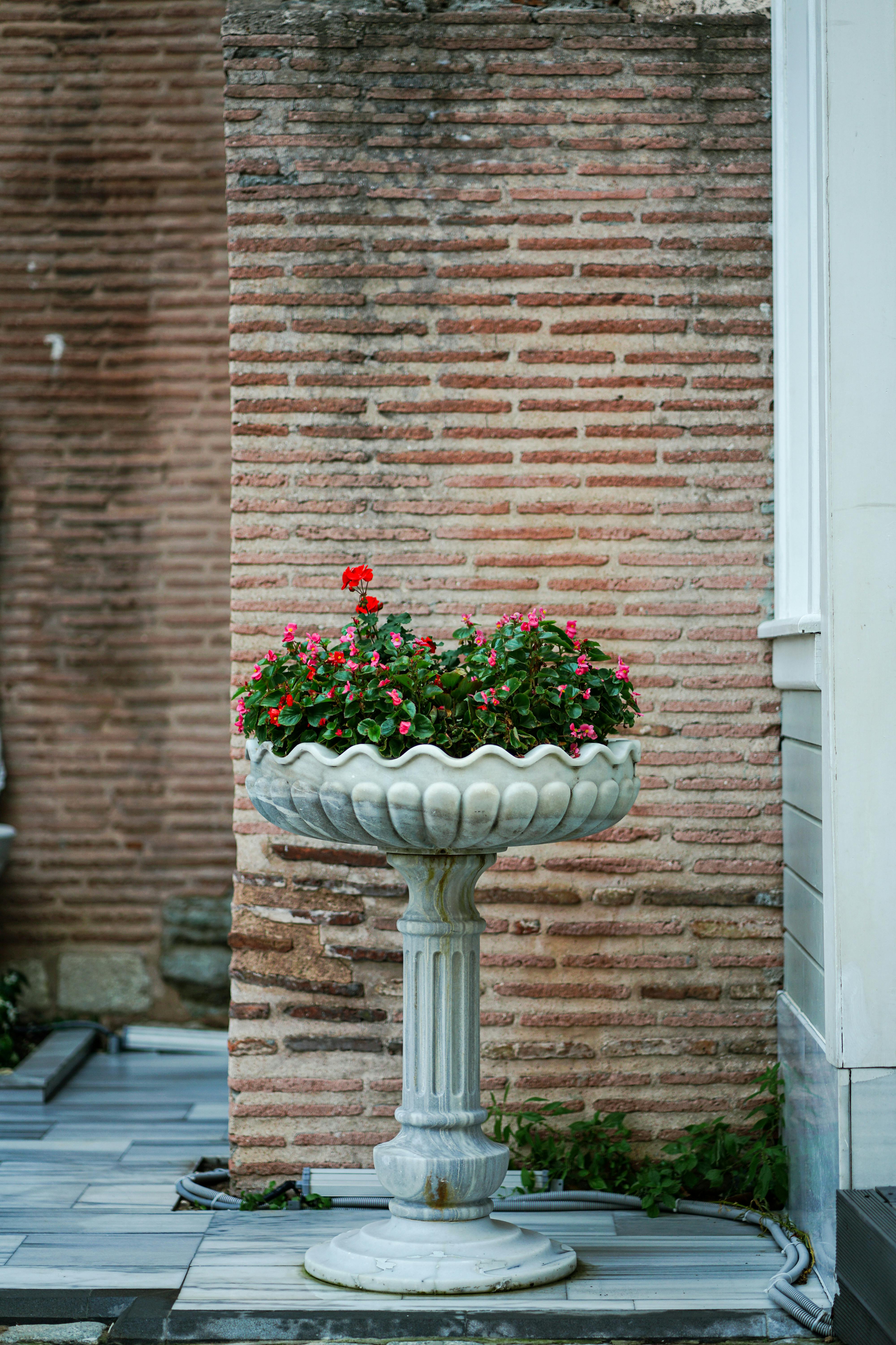 Marble planter with vibrant flowers against a rustic brick wall.