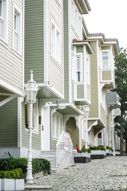 Elegant olive green townhouses line a cobbled street with classic streetlights.