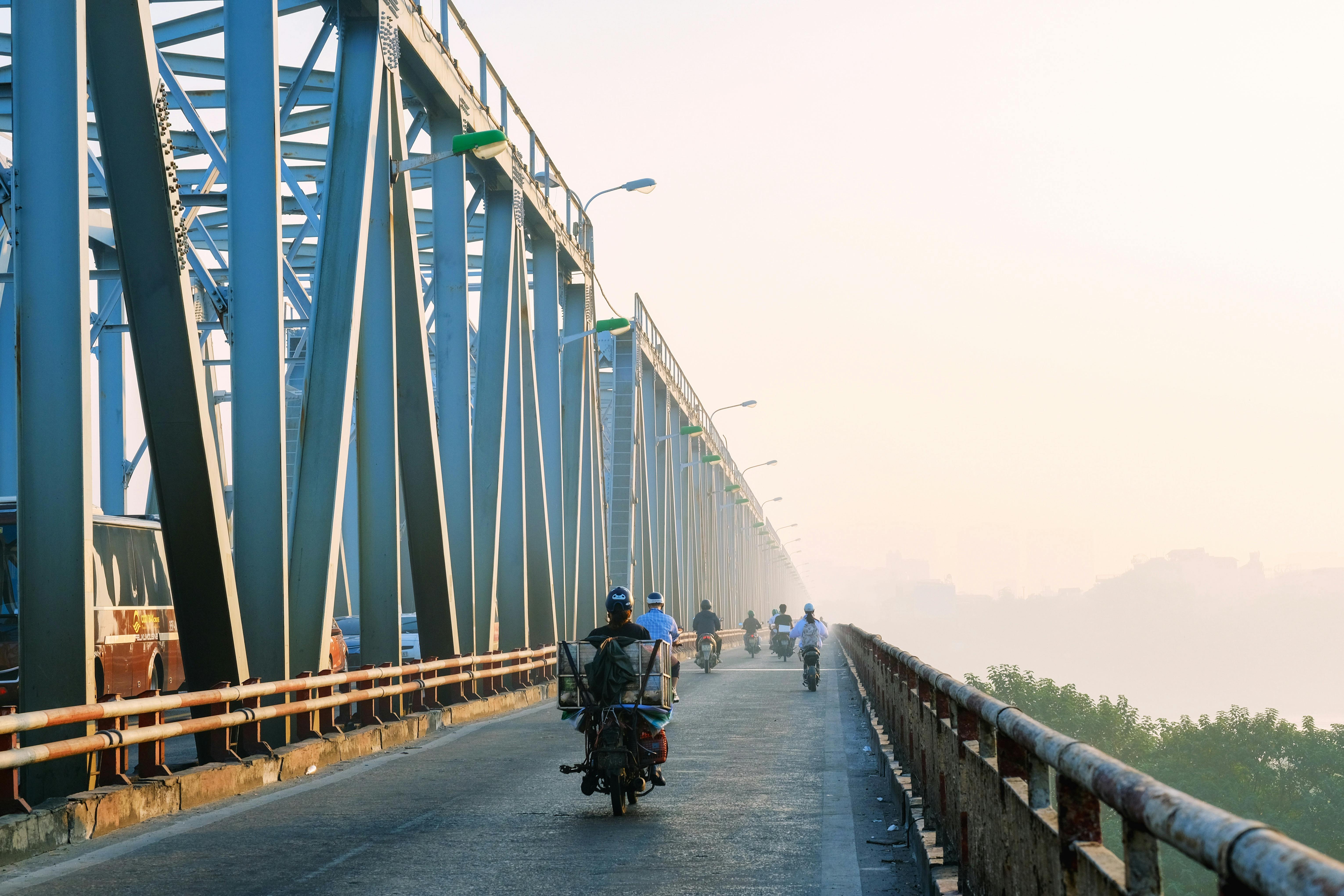Motorcyclists traverse a foggy steel bridge on a misty day, showcasing daily commute.