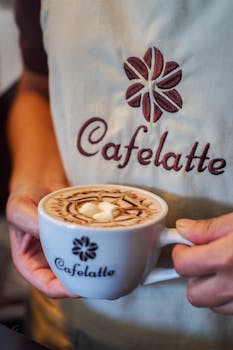 Close-up of a barista holding a beautifully crafted latte with art in a Cafe Latte branded mug.