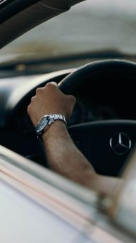 A hand wearing a silver watch grips a Mercedes-Benz steering wheel, showcasing luxury driving in Libya.