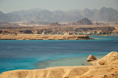 Free Stunning view of a coastal town with rugged mountain backdrop and vibrant blue sea. Stock Photo