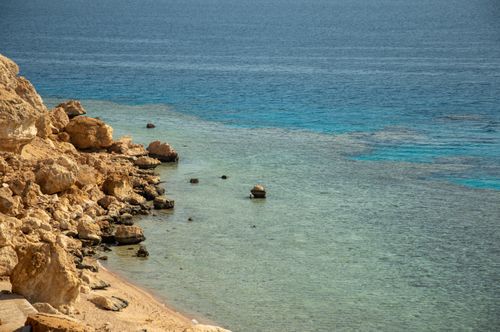Free Beautiful scenic view of a rocky shoreline meeting clear blue ocean waters. Stock Photo