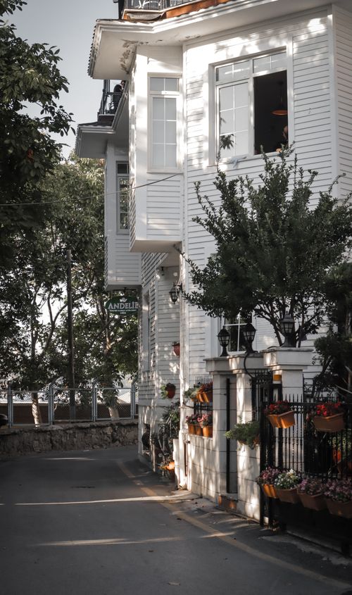 Free Elegant white house with classic architecture and lush greenery along a serene city street. Stock Photo