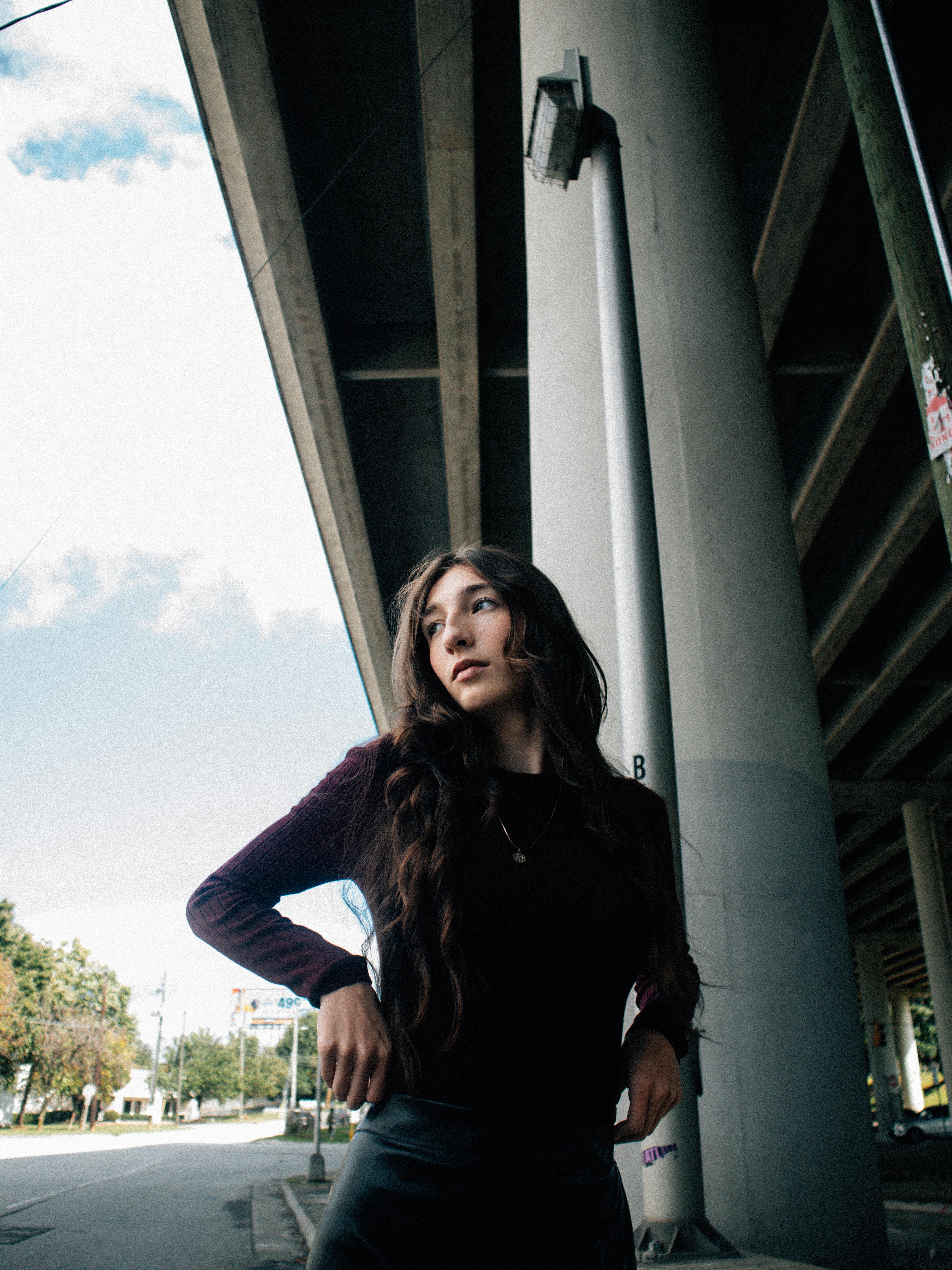 a woman in a black top and leather pants standing under a bridge