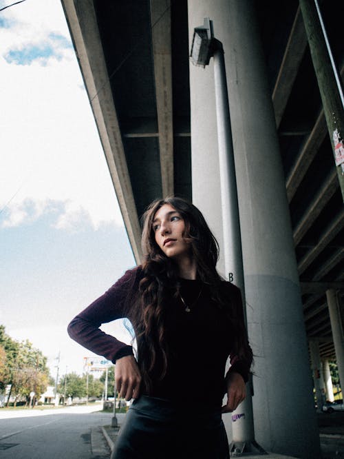 A woman in a black top and leather pants standing under a bridge