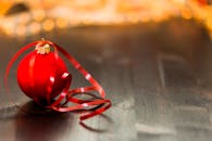 木桌上摆放着带有装饰丝带的红色节日小玩意，背景中灯光模糊