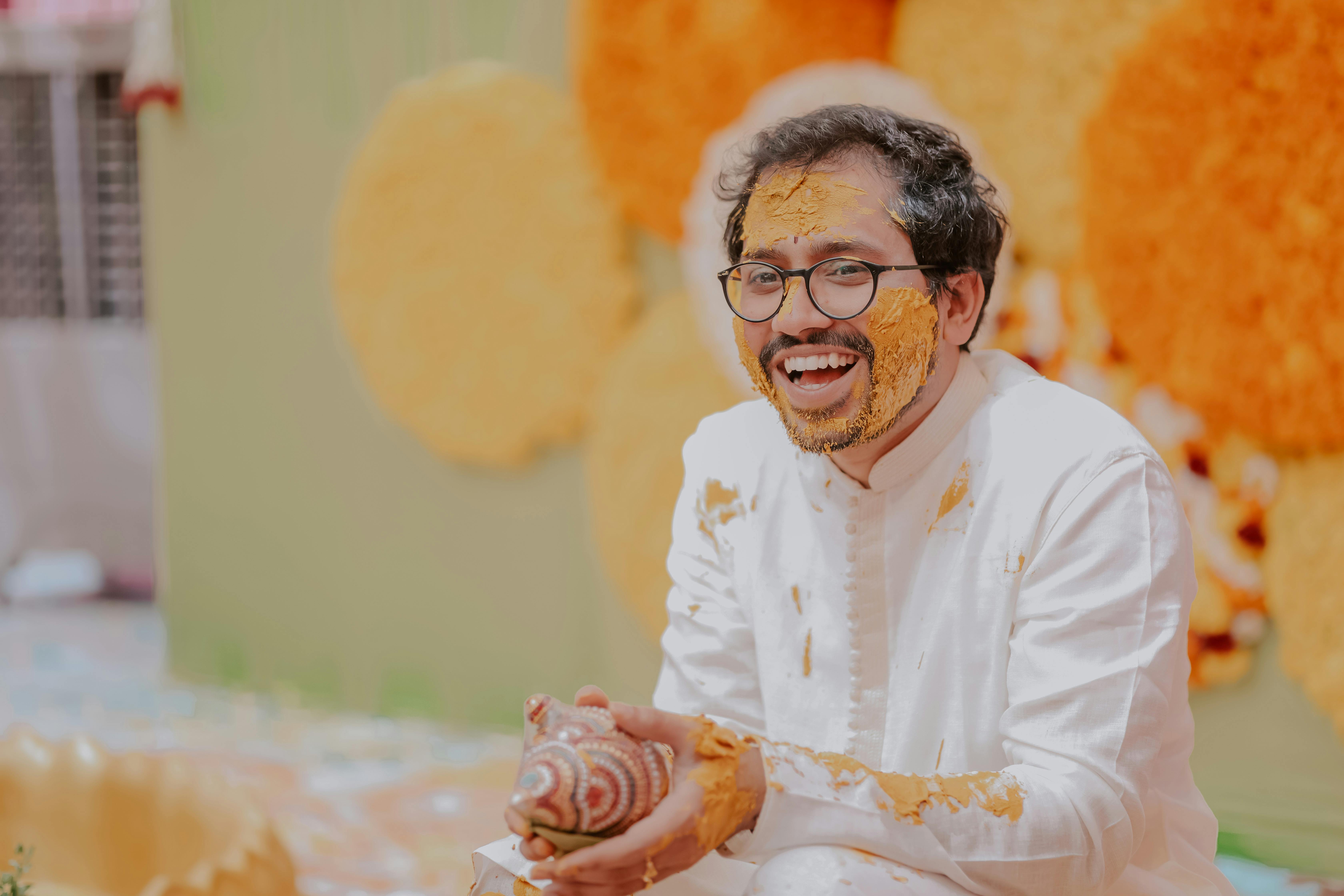 Happy Indian man laughing during traditional Haldi ceremony, covered in turmeric.