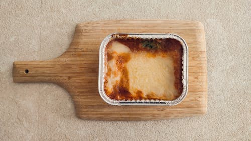 Baked Lasagna in Aluminum Tray on Wooden Board