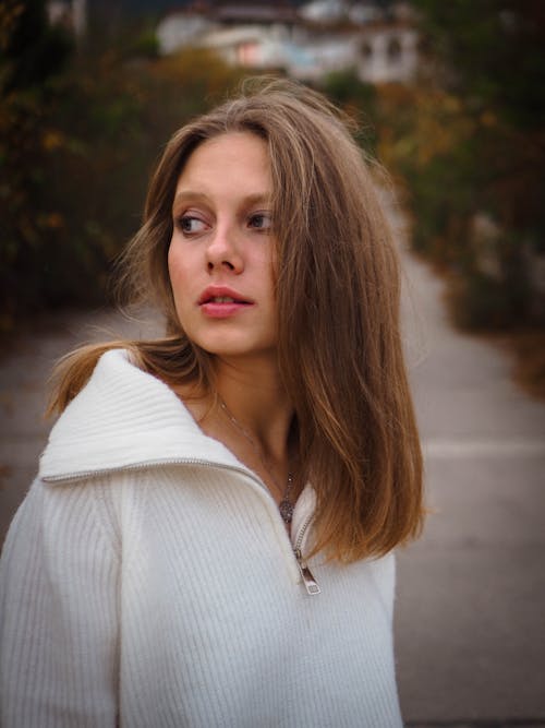 Young Woman in a White Sweater Standing Outside 