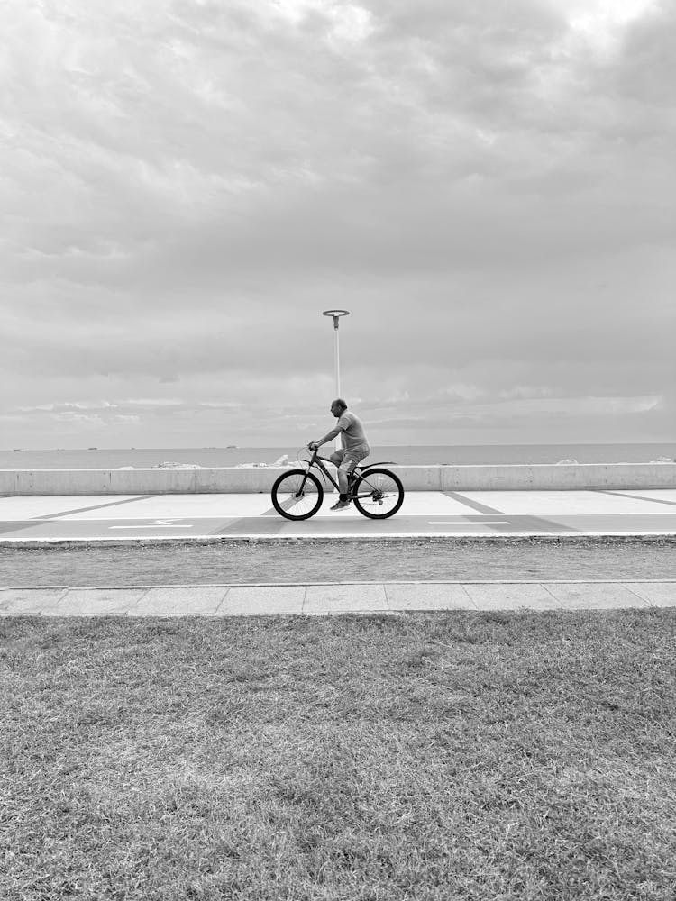 Man Riding Bike On Promenade On Sea Coast In Black And White