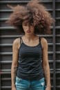 一位留着浓密卷发的年轻女子，身穿休闲黑色背心和牛仔裤