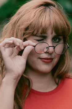 特写肖像中，一位微笑的女人拿着眼镜，俏皮地眨着眼