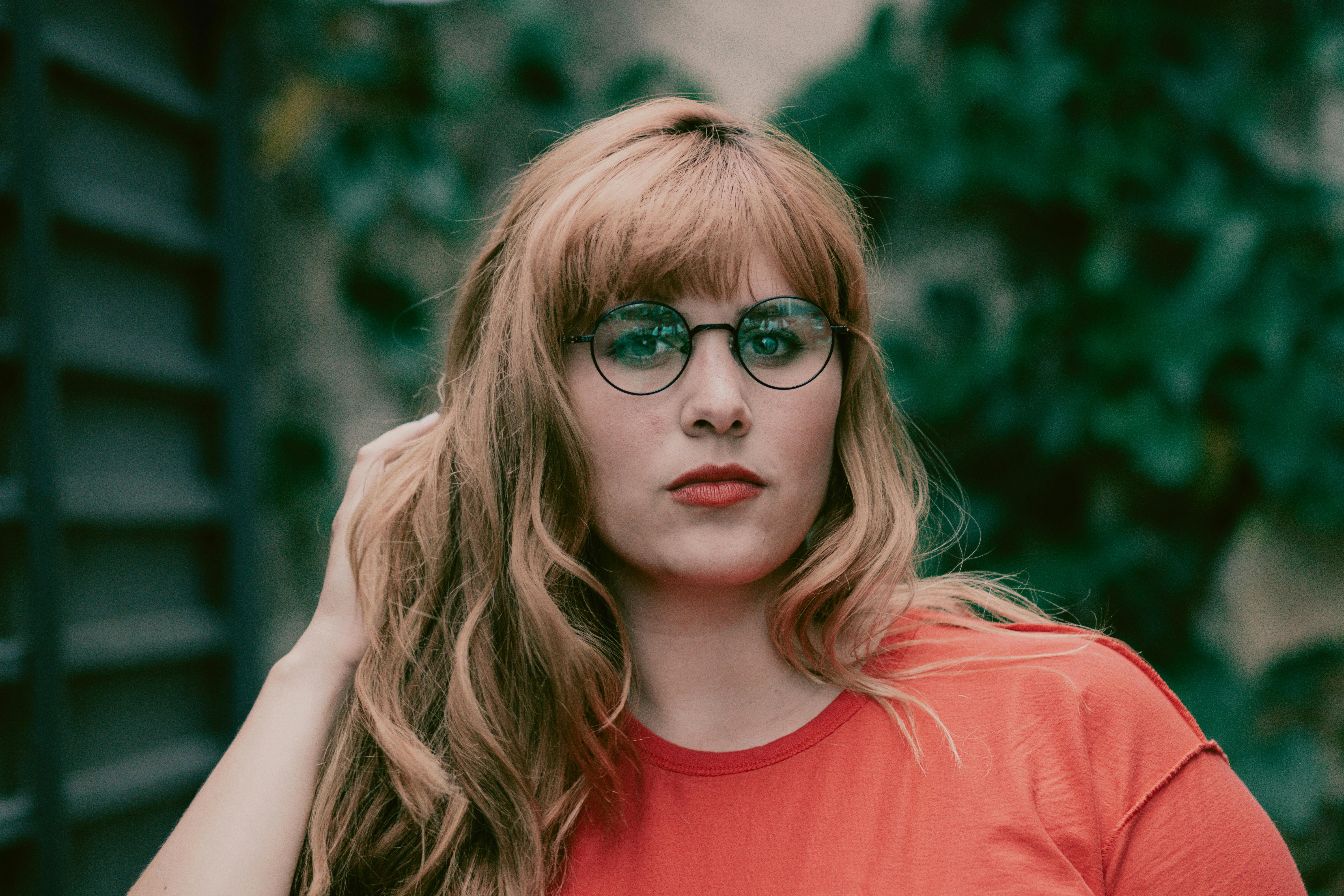 一位戴着眼镜、身穿鲜艳红衫的年轻女子自信地在户外摆姿势