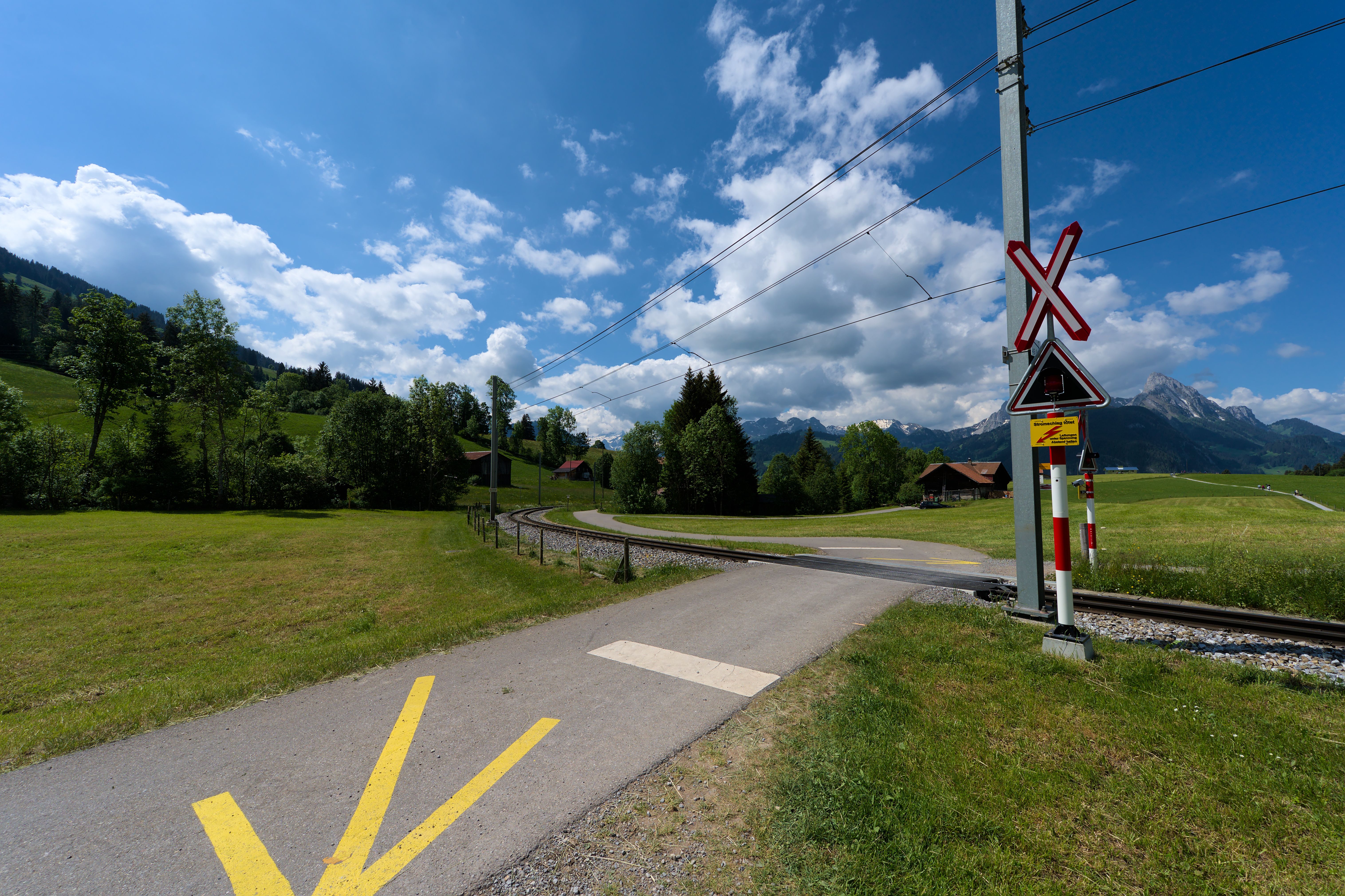 Un passage à niveau pittoresque à Saanen, en Suisse, encadré par les Alpes suisses sous un ciel dégagé.