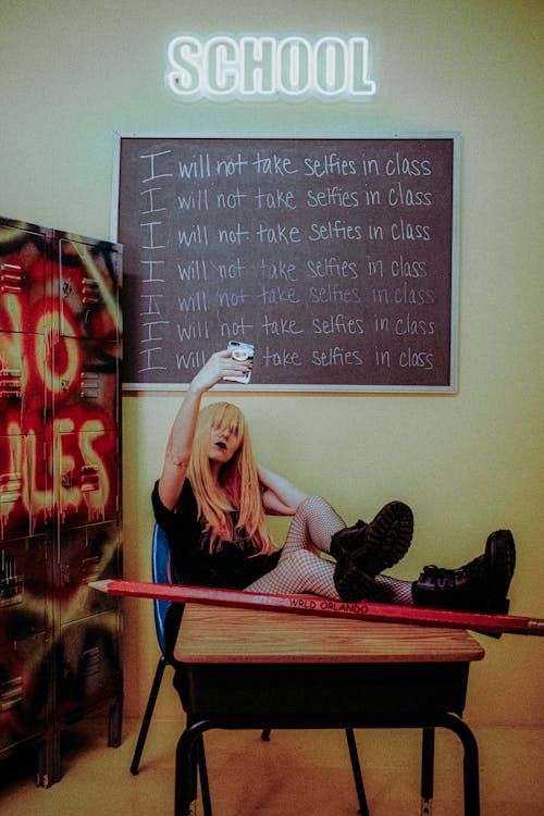 A girl sitting on a chair with a skateboard in front of a chalkboard