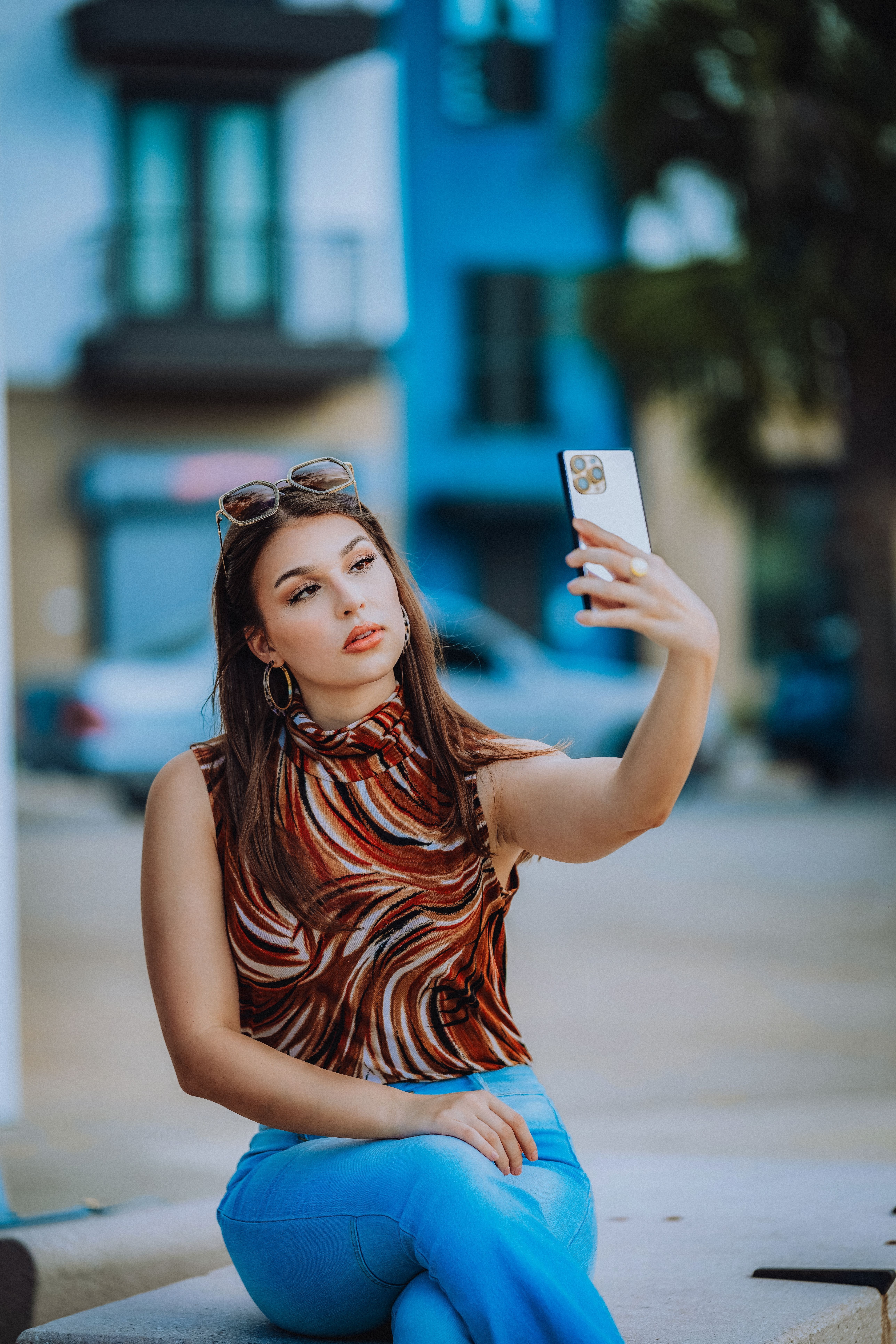 Stylish woman taking a selfie outdoors with a smartphone, sitting elegantly in a vibrant urban setti