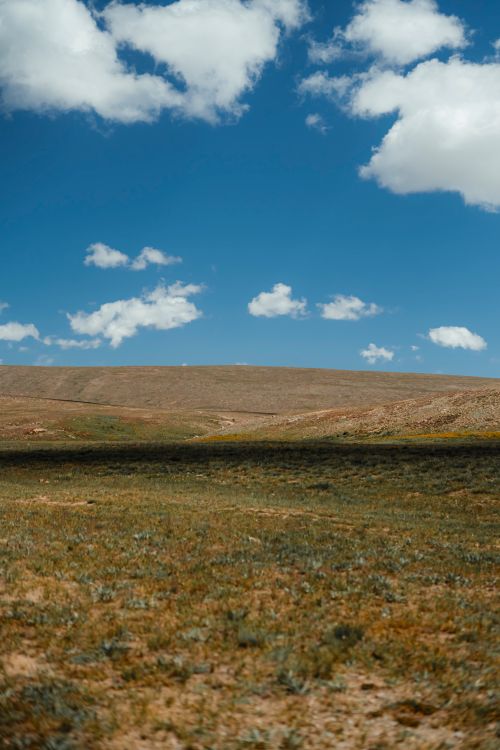 Free A tranquil rural landscape featuring rolling hills and a grassy field beneath a vibrant blue sky. Stock Photo