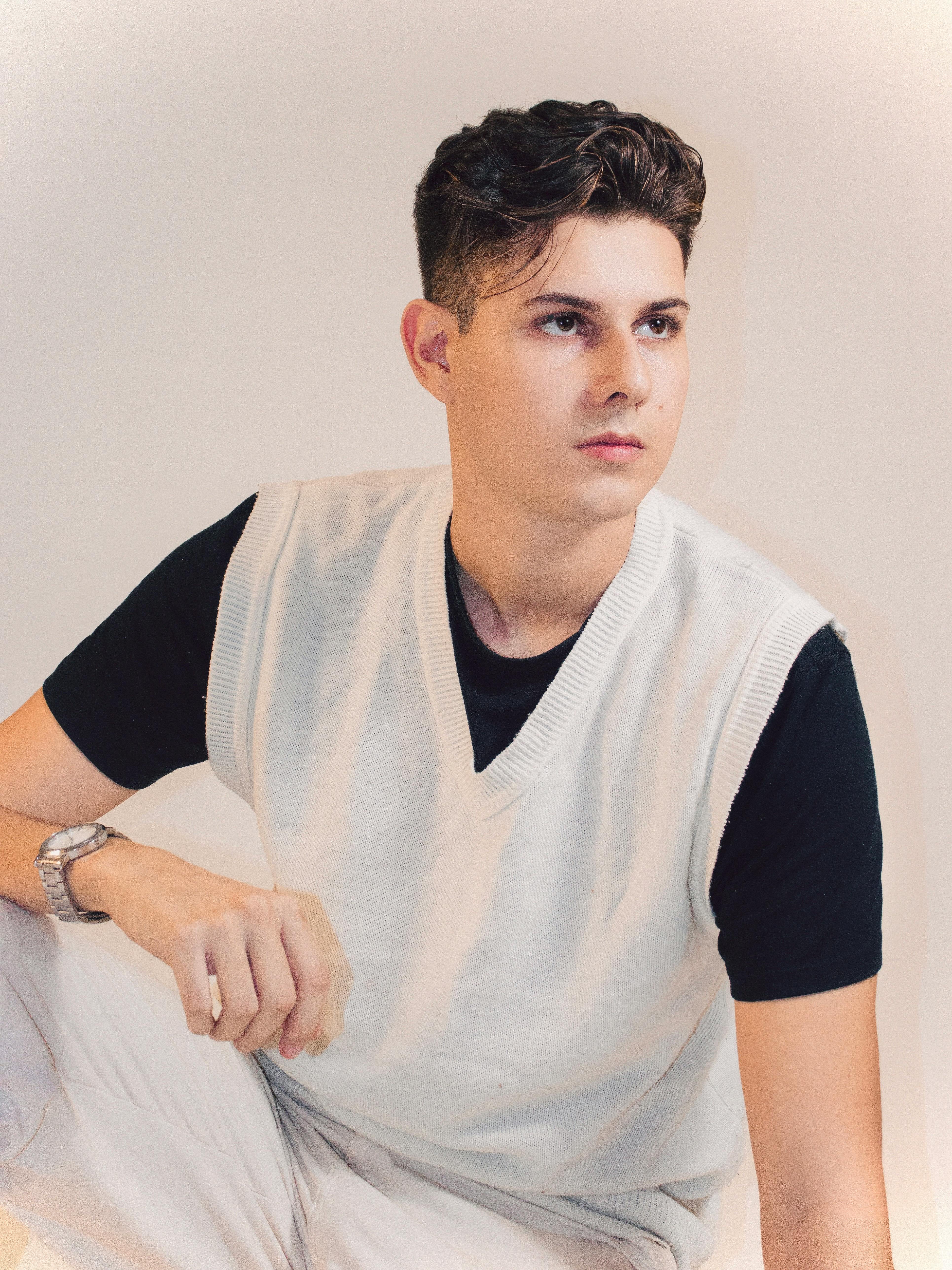 Stylish young man posing in studio wearing a white knitted vest over a black t-shirt.
