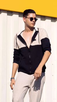 Young man in stylish fashion posing with sunglasses against a bright background.